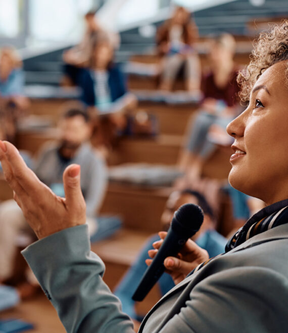 Mid adult businesswoman giving a speech to group of people during a seminar in conference hall.